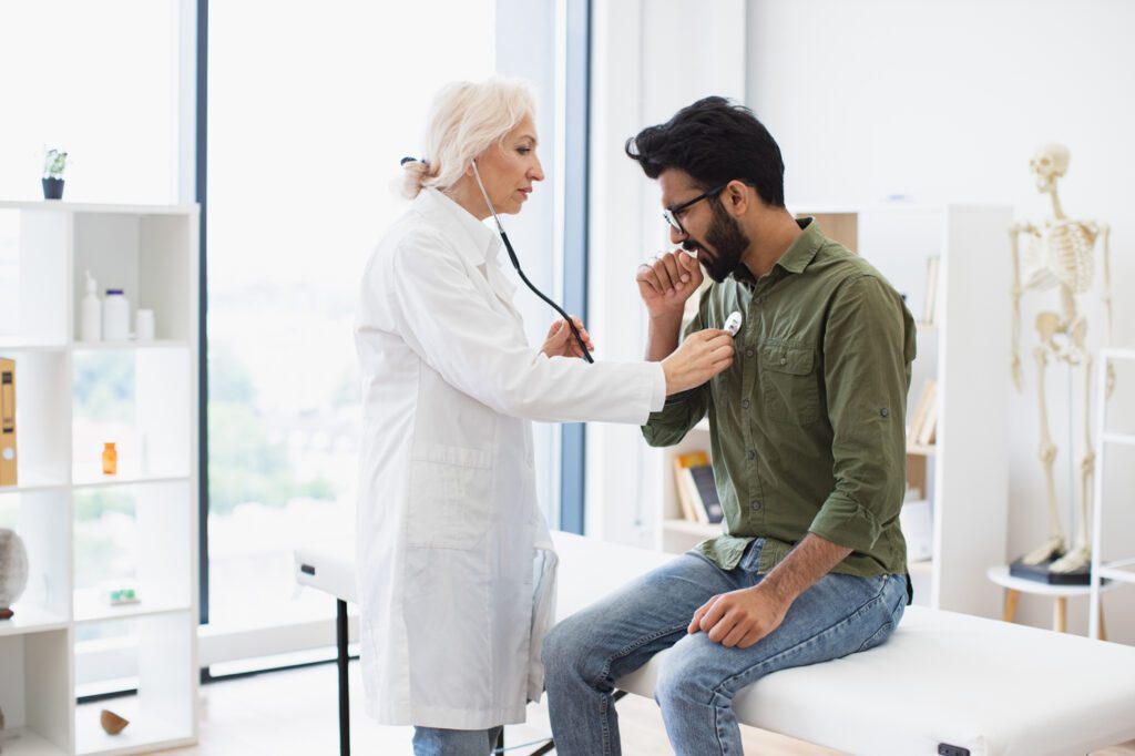 Elderly woman in white lab coat listening to patient's chest with stethoscope.
