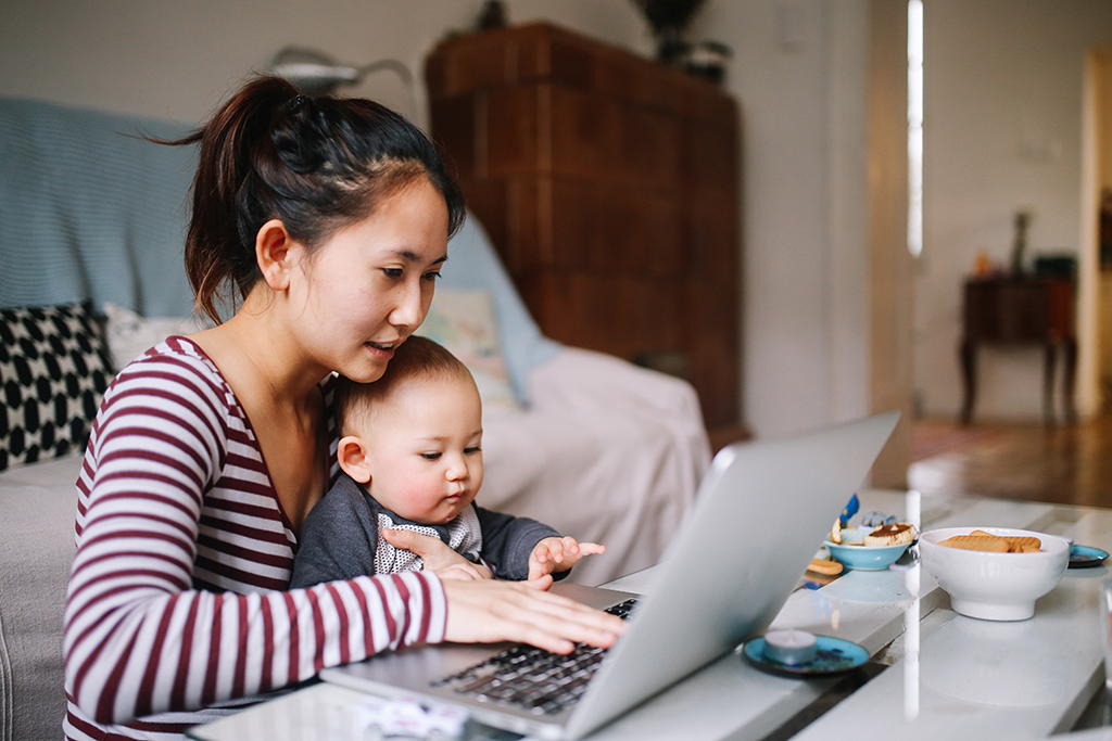 Young Asian mom trying to work on laptop with her baby boy