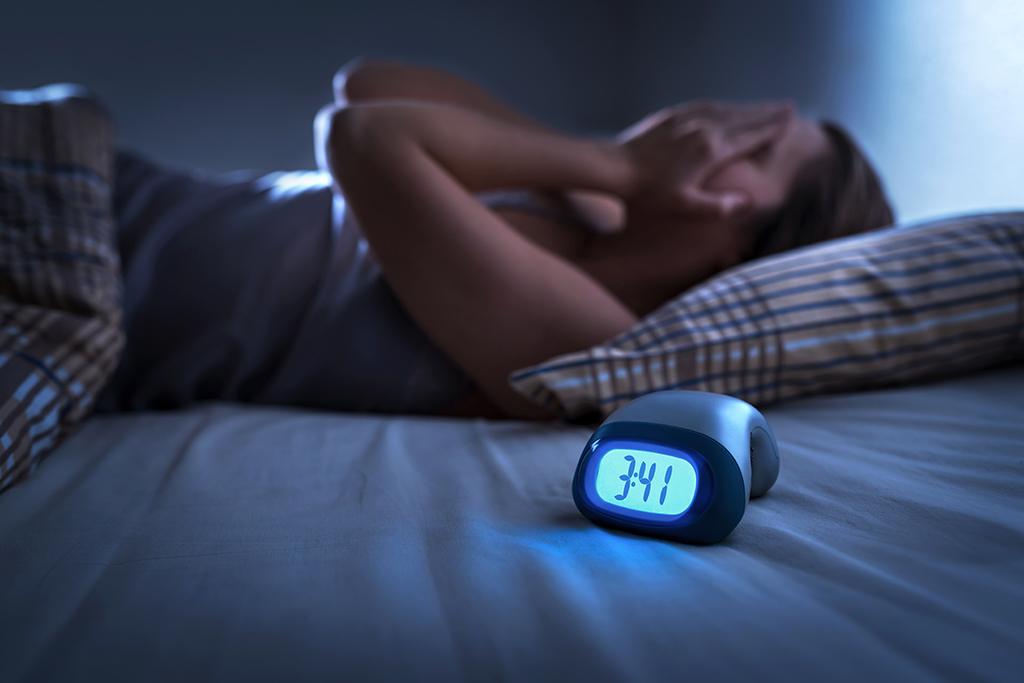 Woman suffering form insomnia in bed next to an alarm clock