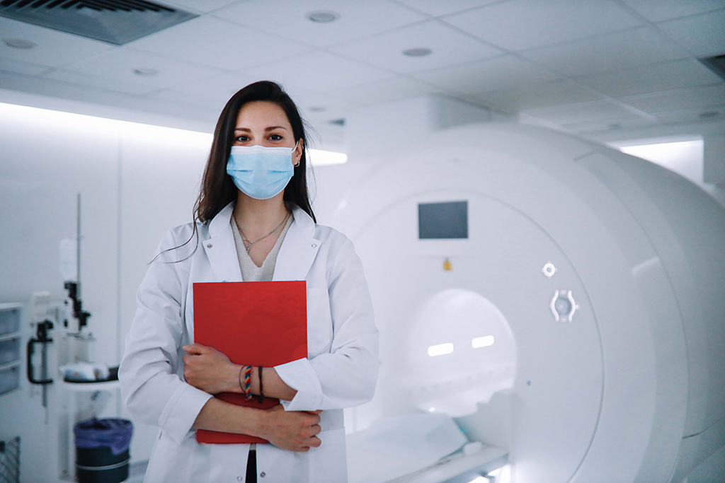 Female medical professional wearing mask standing in front of a MRI machine