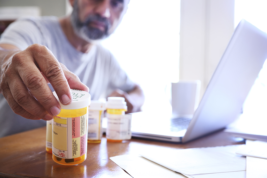 Hispanic Man Sitting At Table Reaches For His Prescription Medications