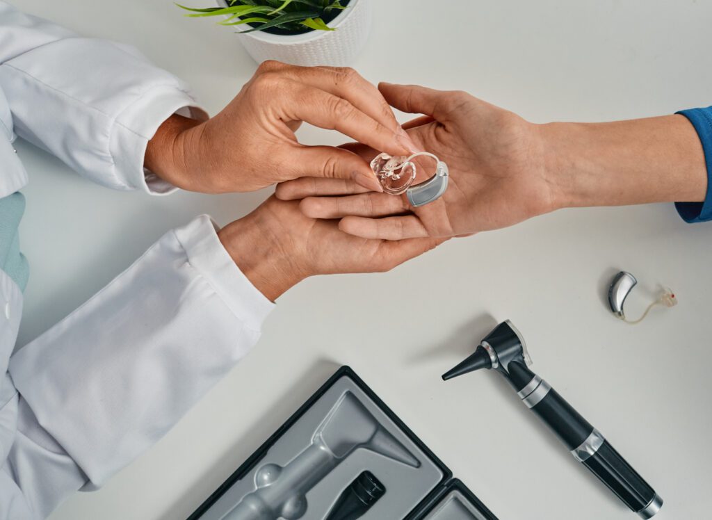 Medical professional placing hearing aid in patient's hand