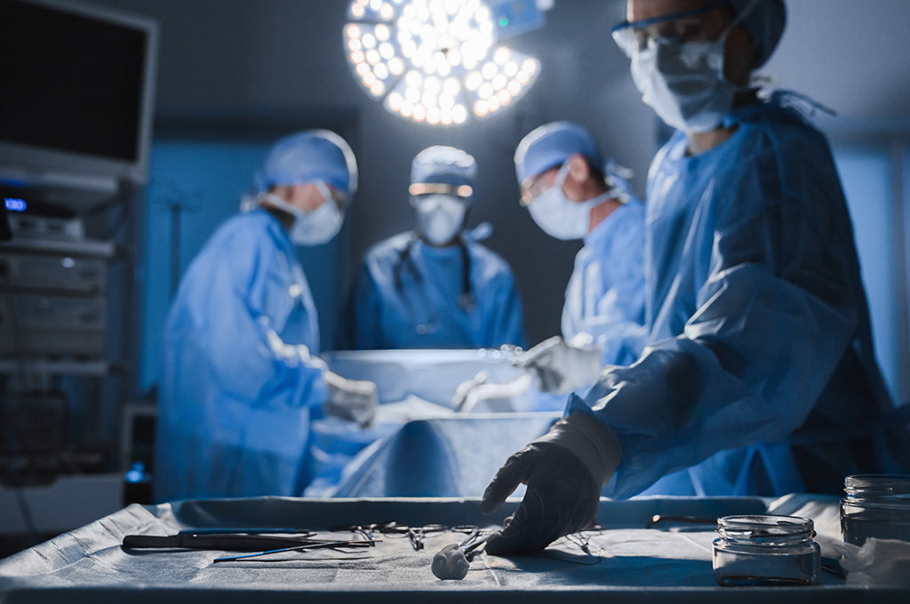 Surgical tools lying on table while group of surgeons at background operating patient
