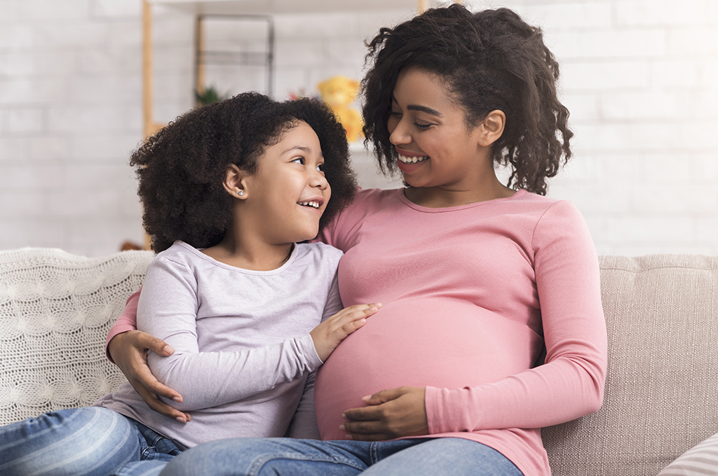 Happy pregnant mother and her cute afro daughter hugging on couch