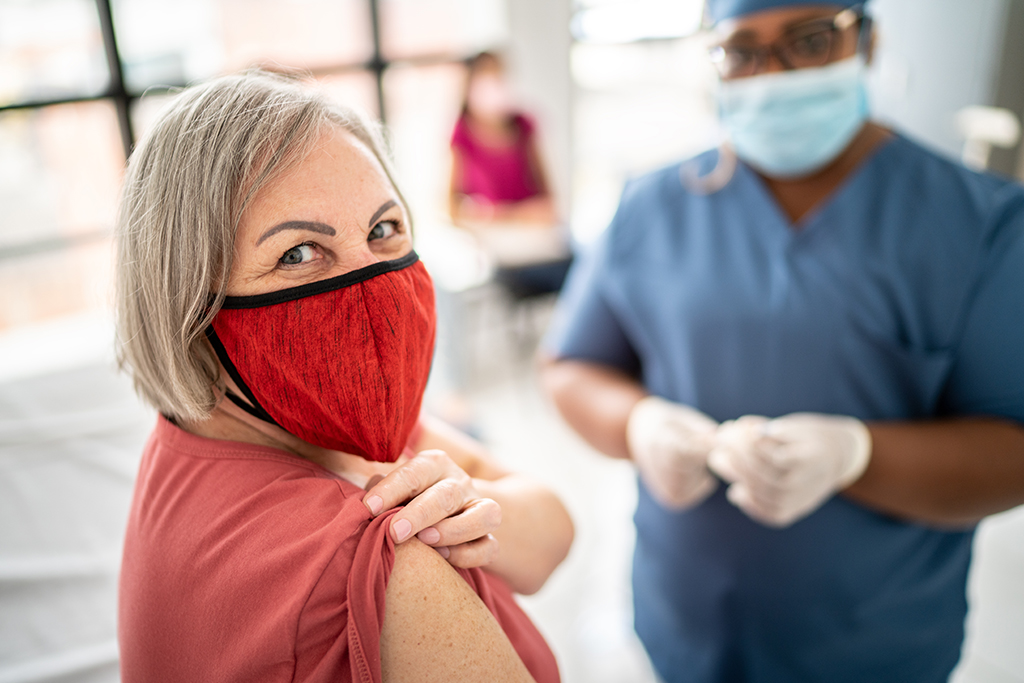 Senior woman showing arm before taking vaccine - wearing face mask