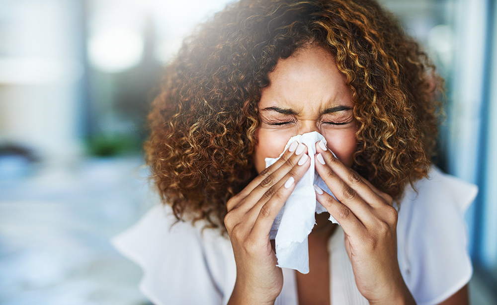 Female sneezing into a tissue at the office