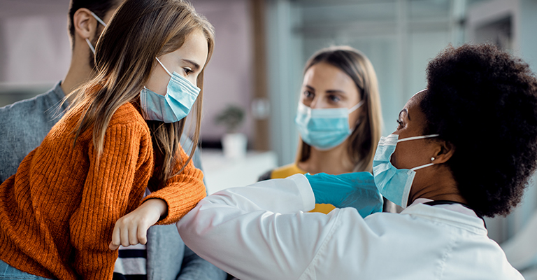 Little girl and African American female doctor elbow bumping at medical clinic.