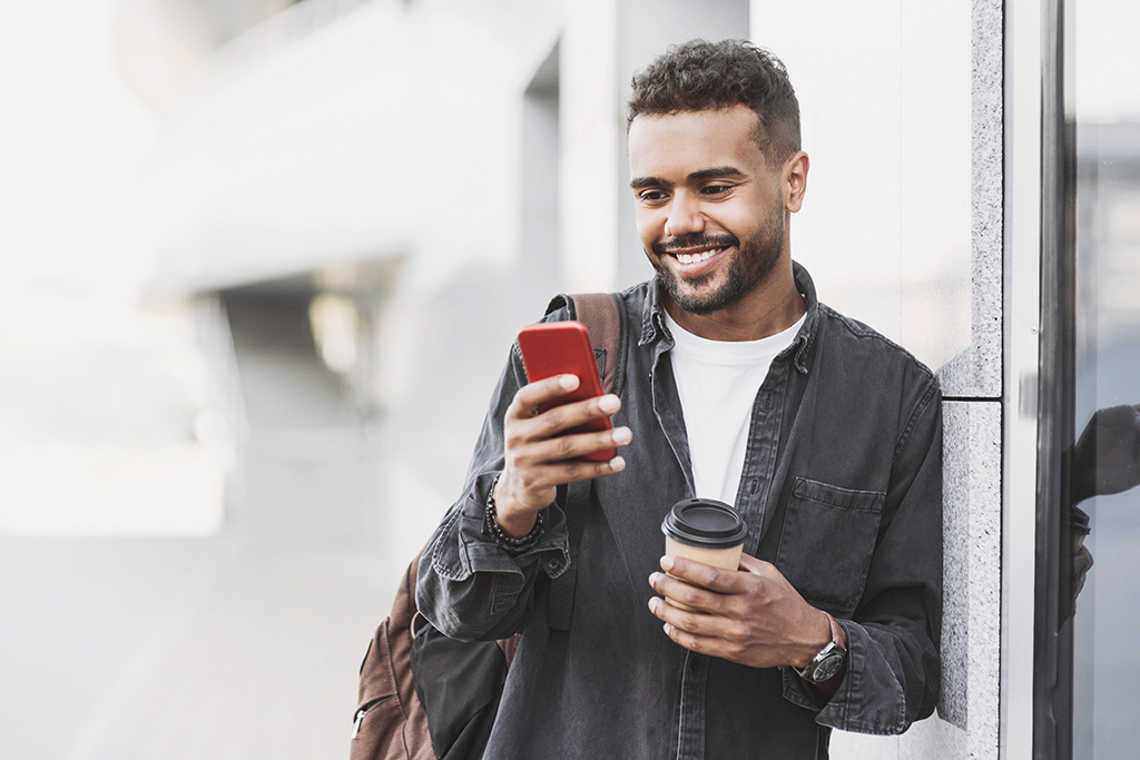 Cheerful young man using smart phone in a city