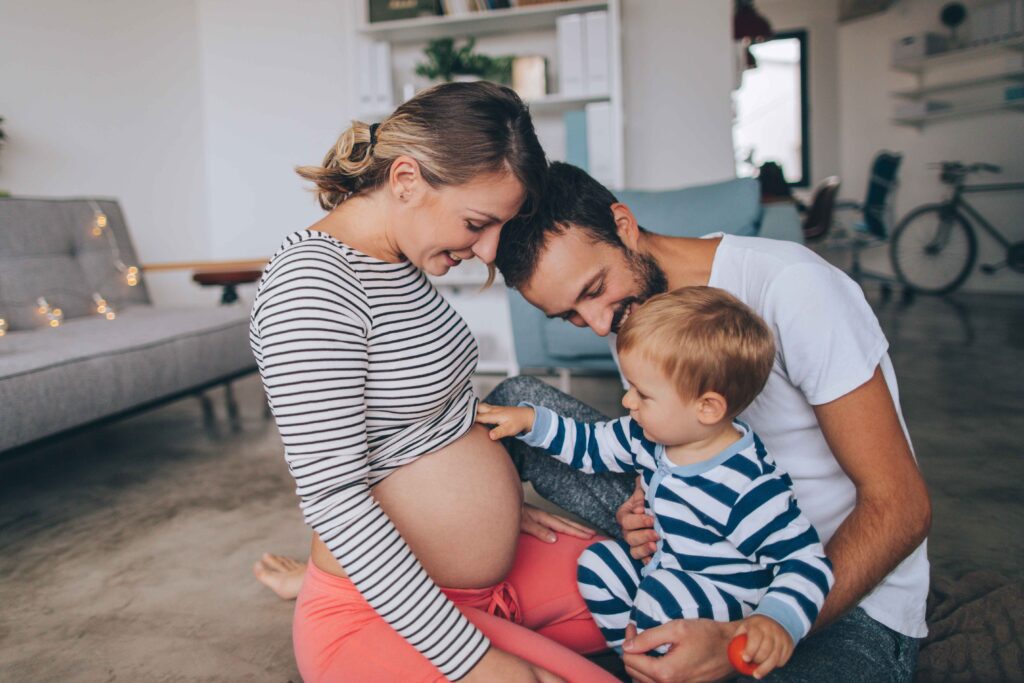 Pregnant woman sitting on the floor with her toddler and husband.