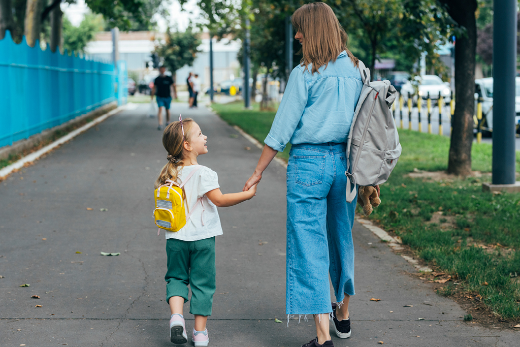 Mother and daughter walking down a sidewalk holding hands