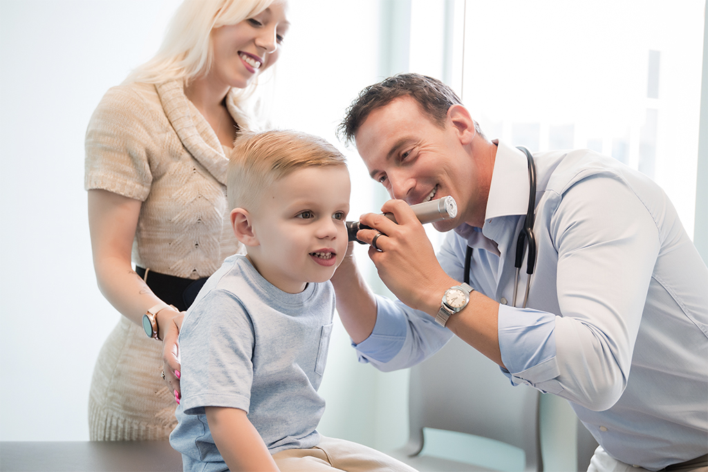 Pediatrician examining ear of little boy