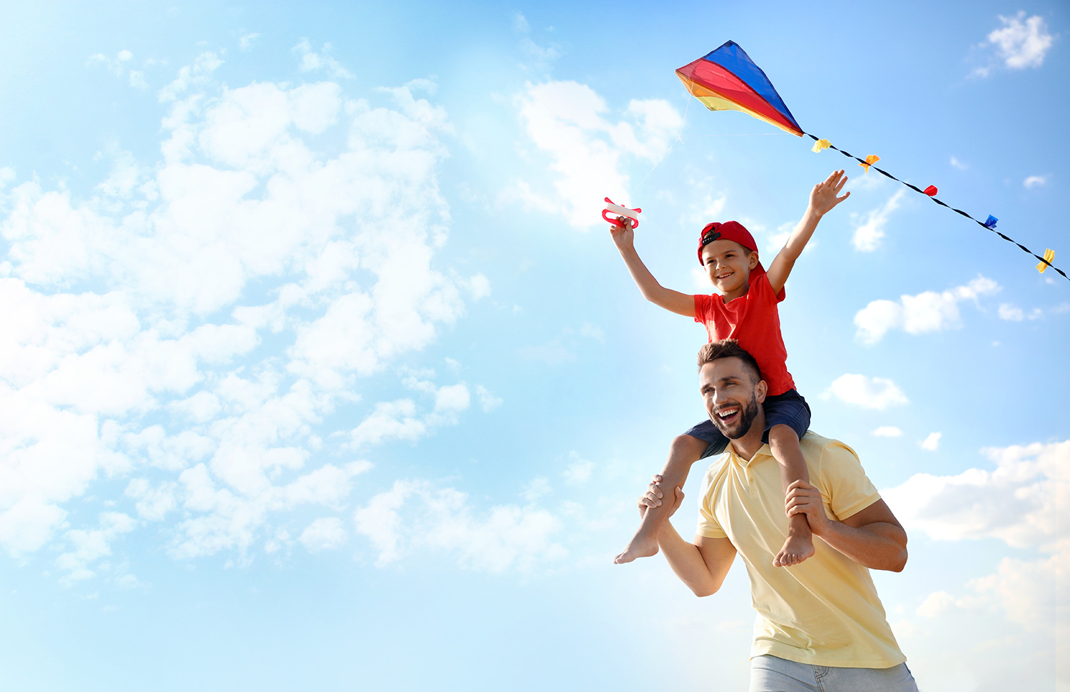 Kid flying a kite while sitting on dad's shoulders