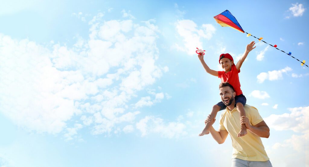Father and son playing with a kite on a blue sky day.